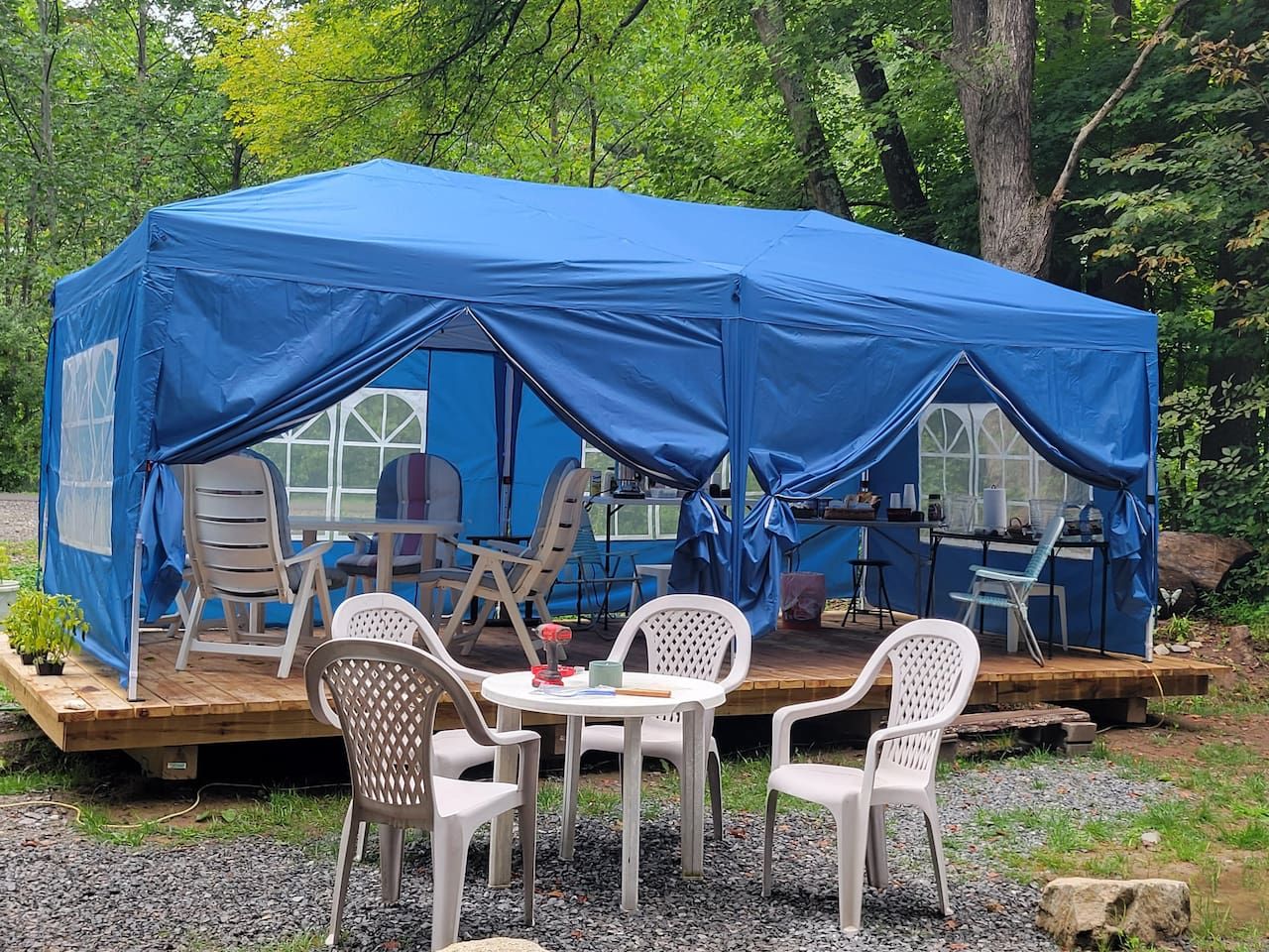 A blue tent with a table and chairs set up on a wooden platform, surrounded by trees.
