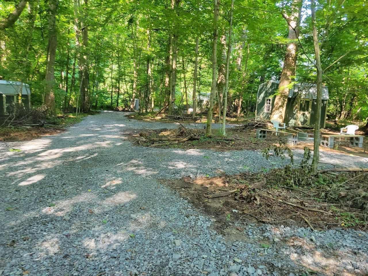 A gravel path in a wooded area with a small structure on the right.