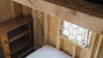 Un lit superposé avec une tête de lit en bois, une fenêtre ornée de rideaux à motifs et une étagère en bois.