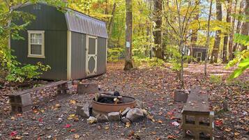 A rustic cabin with a fire pit and benches in a forested area.