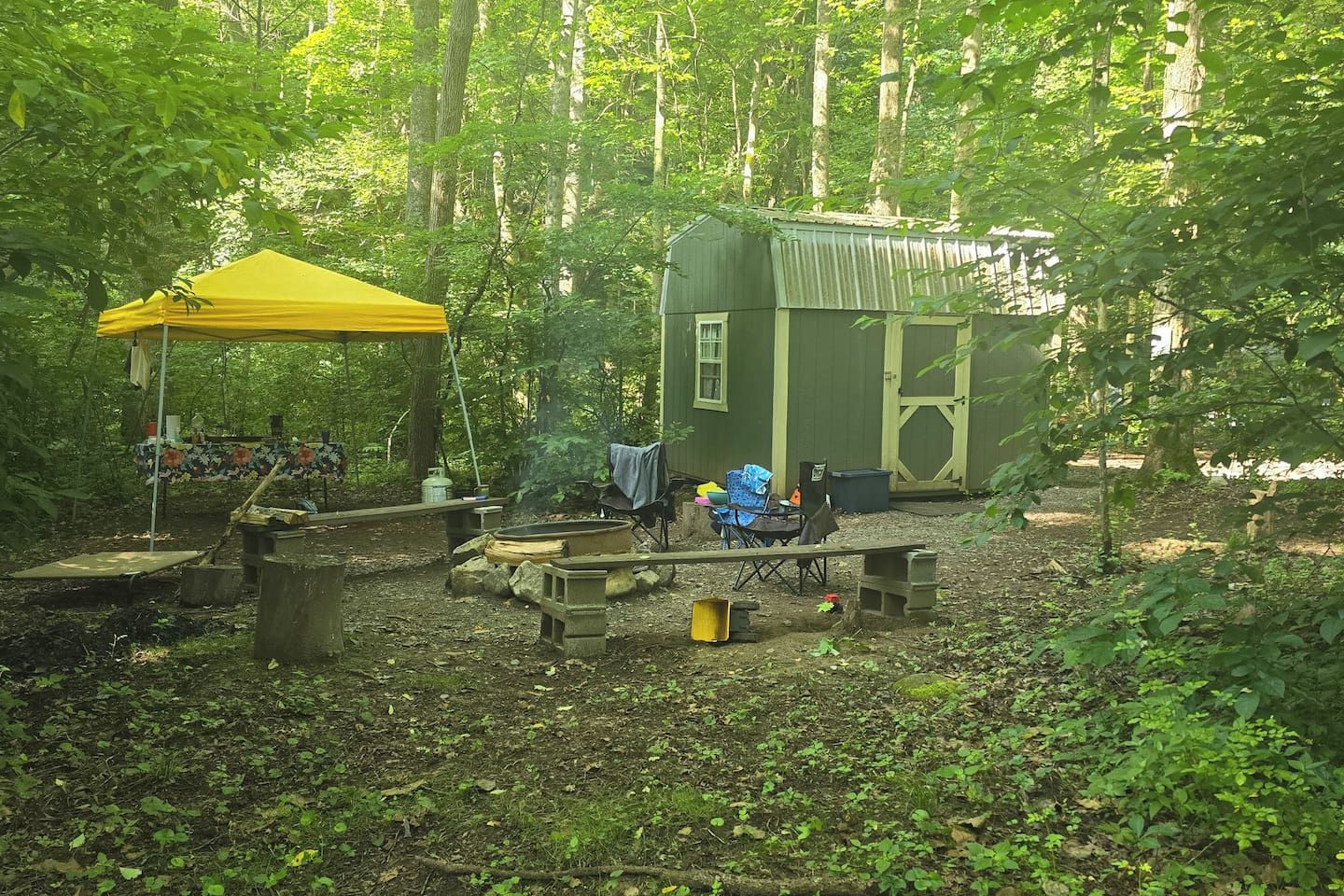 A campsite with a yellow tent, a small cabin, and a picnic table.