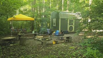 A campsite with a yellow tent, a small cabin, and a picnic table.