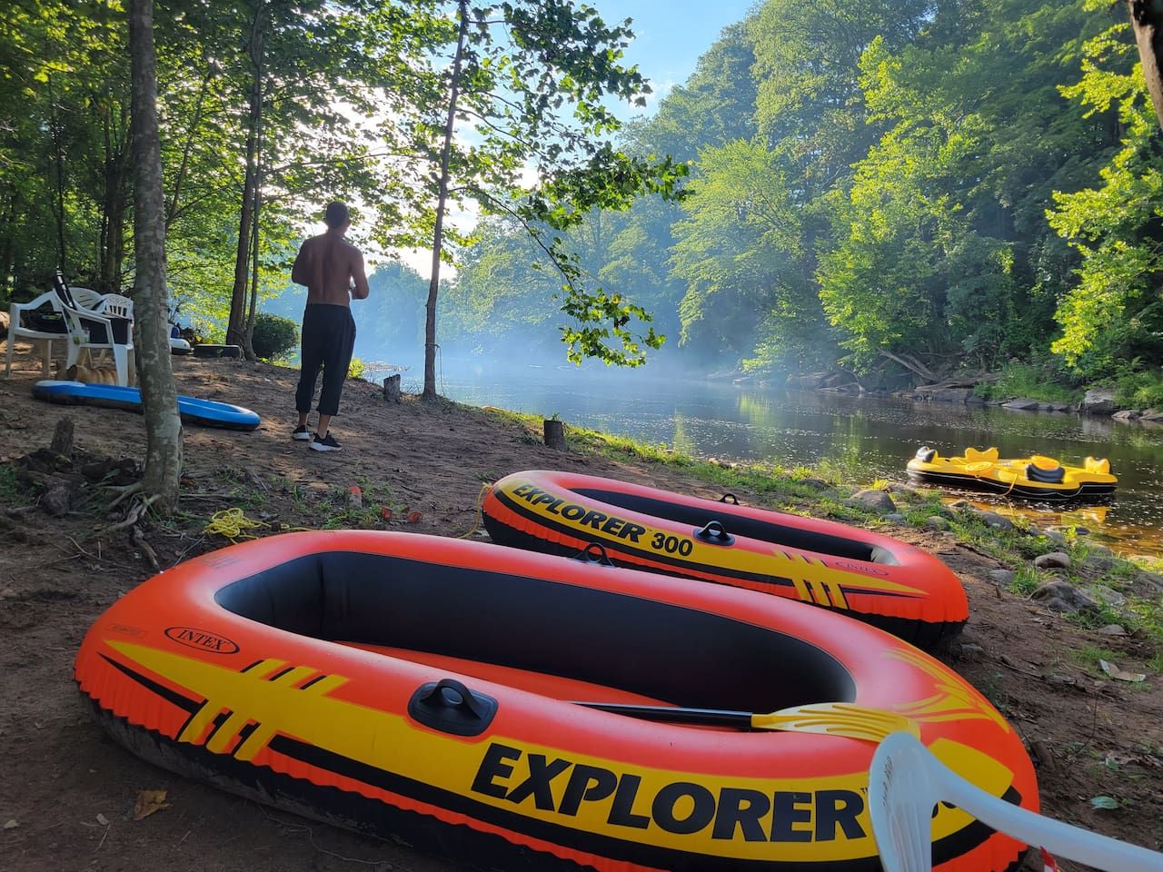 Two inflatable rafts labeled 'EXPLORER 300' and 'EXPLORER' on a sandy shore with trees and a body of water in the background.