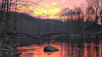 A river with a rock in the middle, surrounded by trees and a sunset sky.