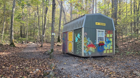 A small, colorful shed labeled 'St. George' in a forested area with a gravel path. - The St. George - Cabin CB5 electric/heat (Parsons)