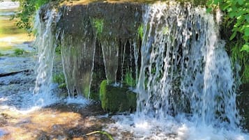 A waterfall cascading over a moss-covered rock structure surrounded by lush greenery.