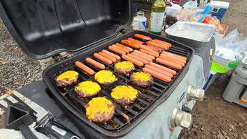 A portable grill with hot dogs and burgers being cooked.
