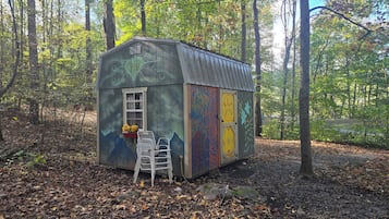 A small wooden shed with a window and a door, surrounded by a forest.