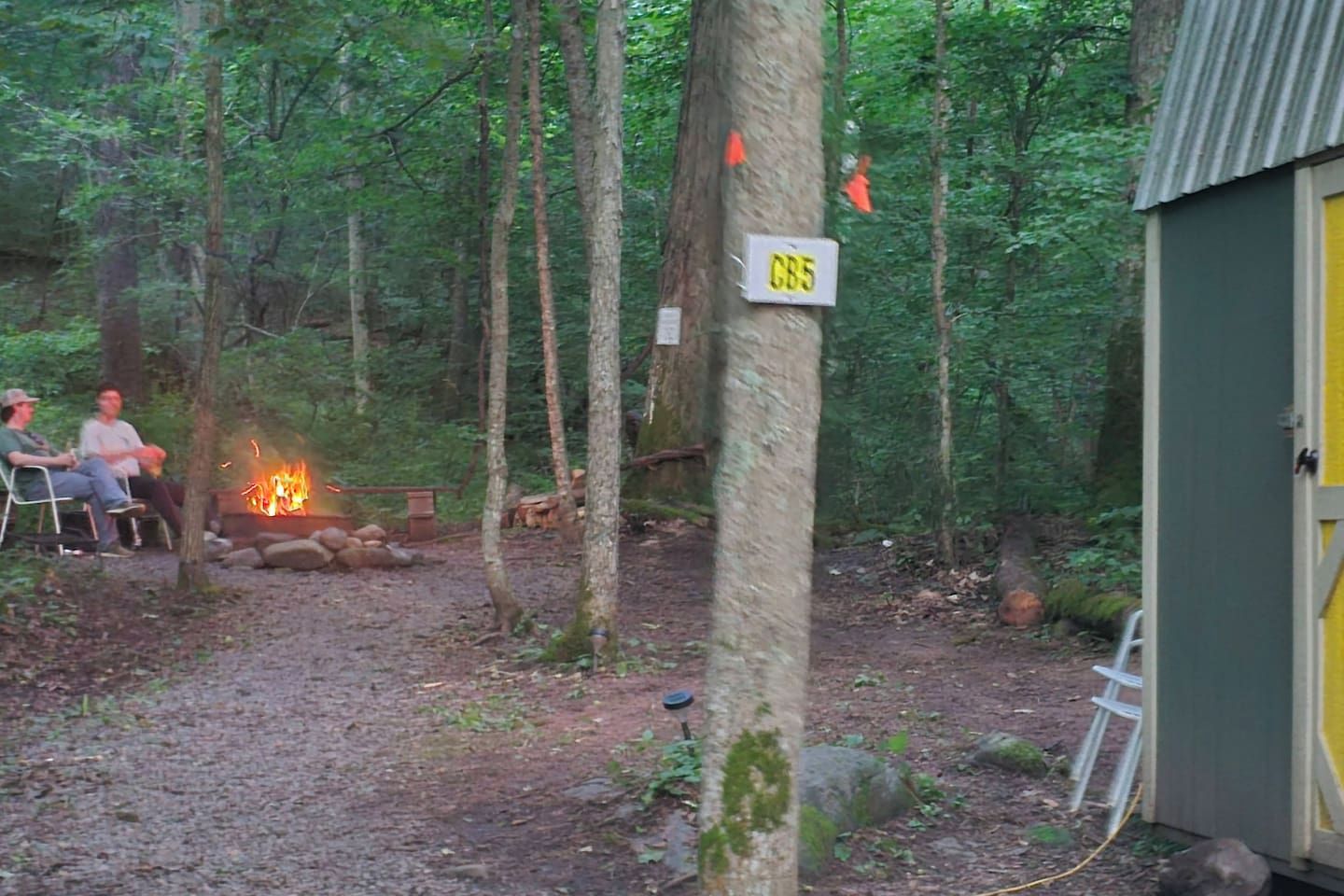 A forested campsite with a fire, a chair, and a sign labeled 'CB5'.