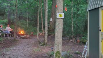 A forested campsite with a fire, a chair, and a sign labeled 'CB5'.