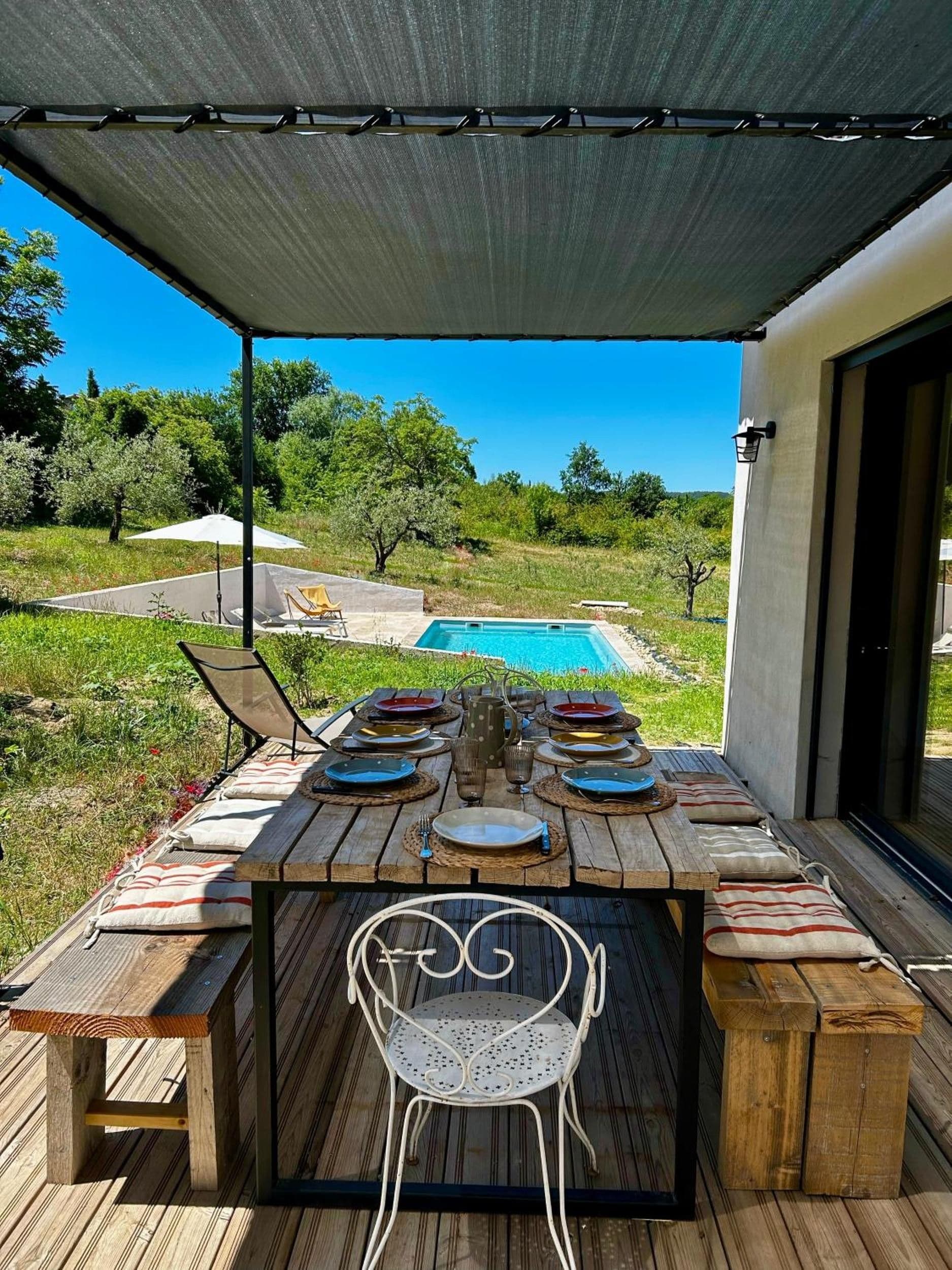 An outdoor dining area with a pool view, wooden table, metal chairs, and a covered patio.