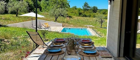 An outdoor dining area with a pool view, wooden table, metal chairs, and a covered patio.