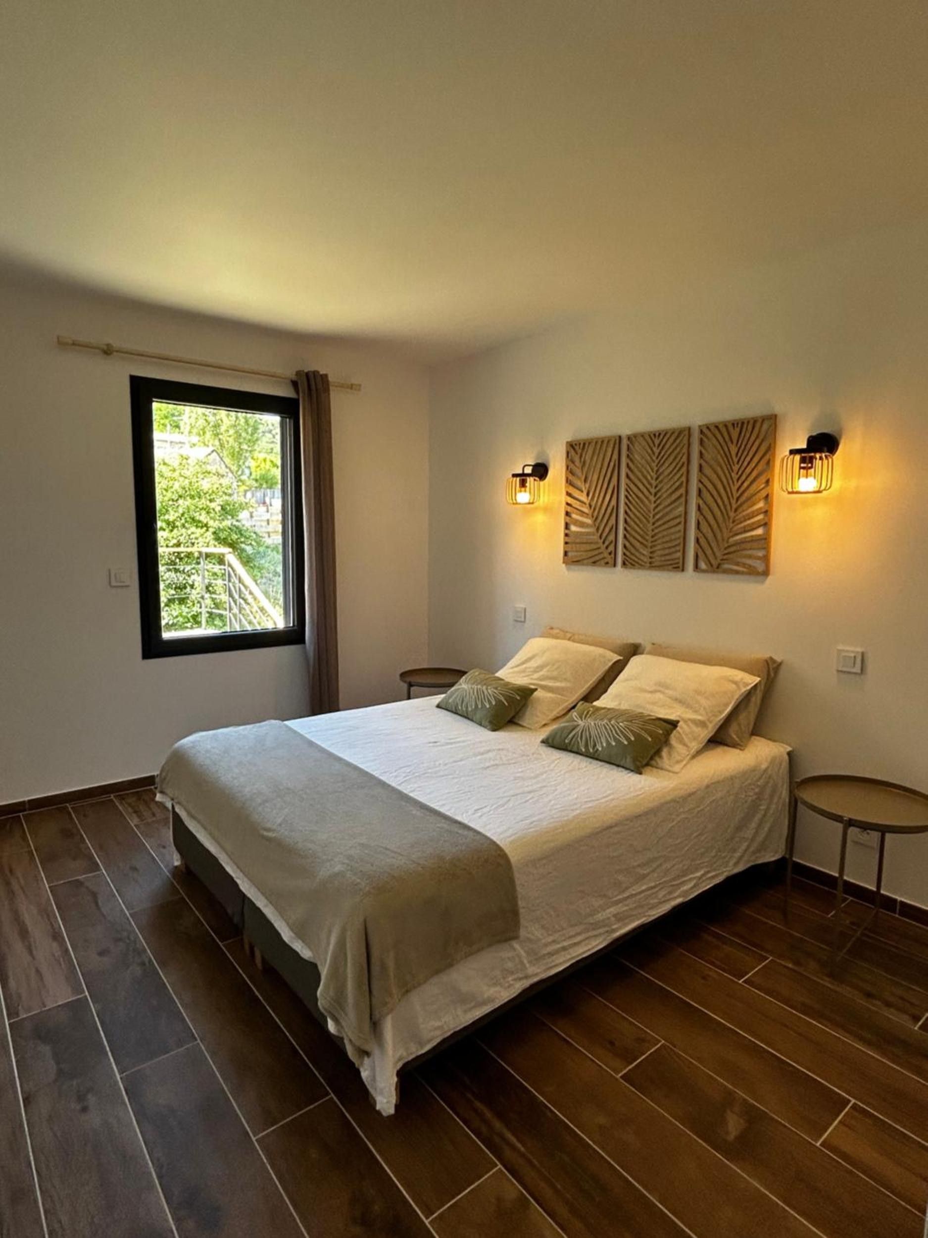 Une chambre à coucher avec un grand lit, deux tables de chevet, une fenêtre avec des rideaux et des luminaires fixés au mur.