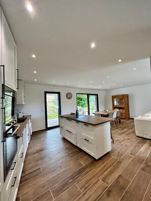 A modern kitchen with a central island, wooden flooring, and a dining area with a table and chairs. - Villa 'Loan' with Private Terrace, Wi-Fi and Air Conditioning (Mollans-sur-Ouvèze)