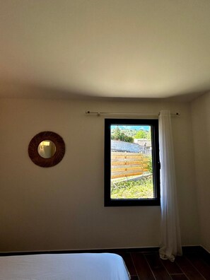 A bedroom with a single bed, a window with a view of a fenced outdoor area, and a wall-mounted mirror. - Villa 'Loan' with Private Terrace, Wi-Fi and Air Conditioning (Mollans-sur-Ouvèze)