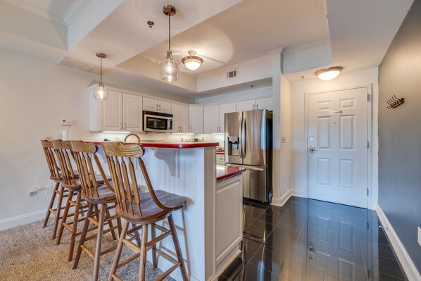 A modern kitchen with white cabinets, a stainless steel refrigerator, and a bar area with wooden chairs.