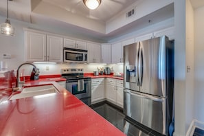 A modern kitchen with white cabinetry, stainless steel appliances, and a red countertop.