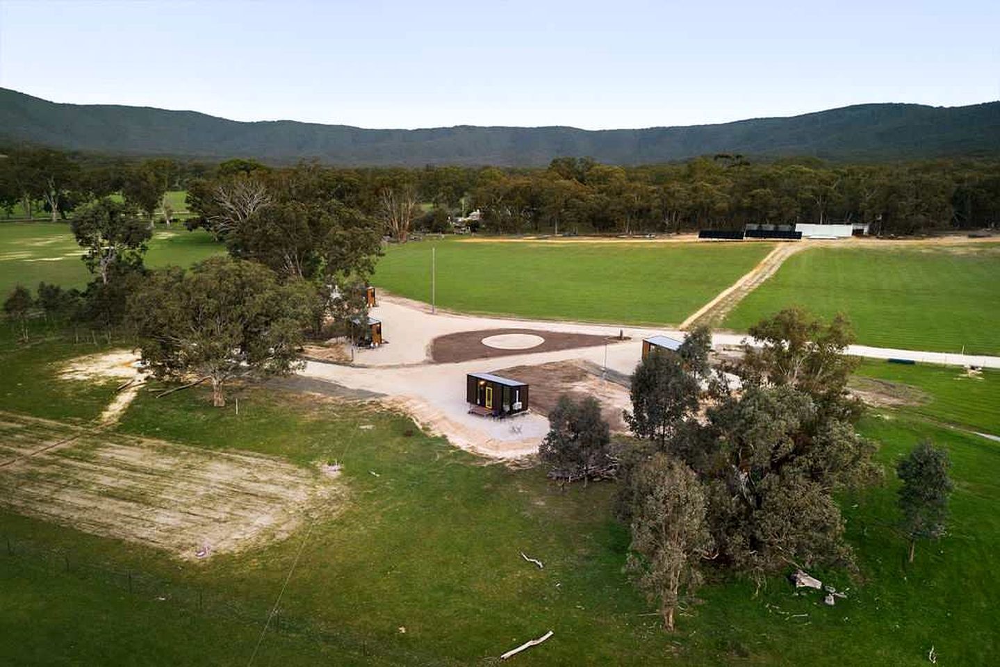 Una propiedad rural con un campo extenso, un edificio pequeño y un camino de tierra.
