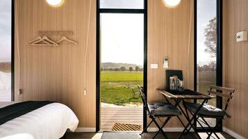 Ein Schlafzimmer mit einem Bett, einem Schreibtisch mit Stuhl und Blick auf ein grünes Feld durch ein großes Fenster.