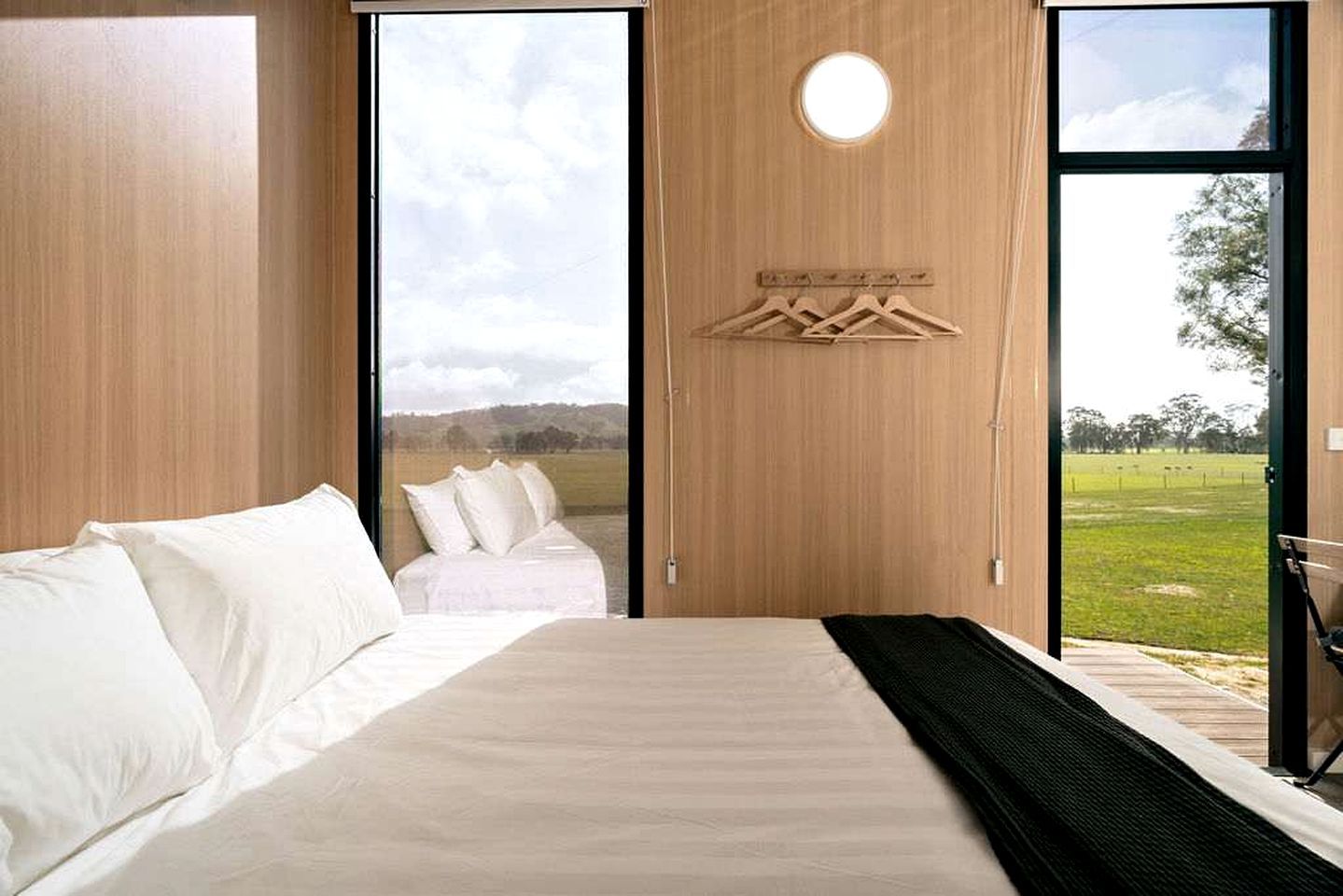 Una camera da letto con un letto, un appendiabiti e vista su un prato attraverso una grande finestra.