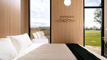Una camera da letto con un letto, un appendiabiti e vista su un prato attraverso una grande finestra.