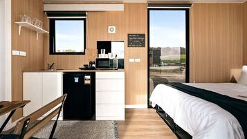 A compact room with a bed, a small kitchenette, a window, and a view of the outdoors.