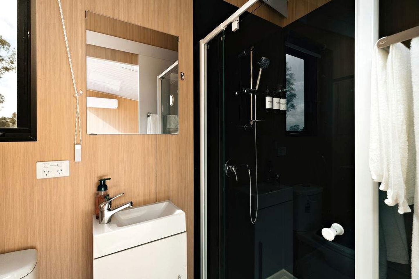 A modern bathroom with a wooden vanity, a glass shower enclosure, and a white towel hanging on the door.