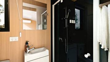 A modern bathroom with a wooden vanity, a glass shower enclosure, and a white towel hanging on the door.