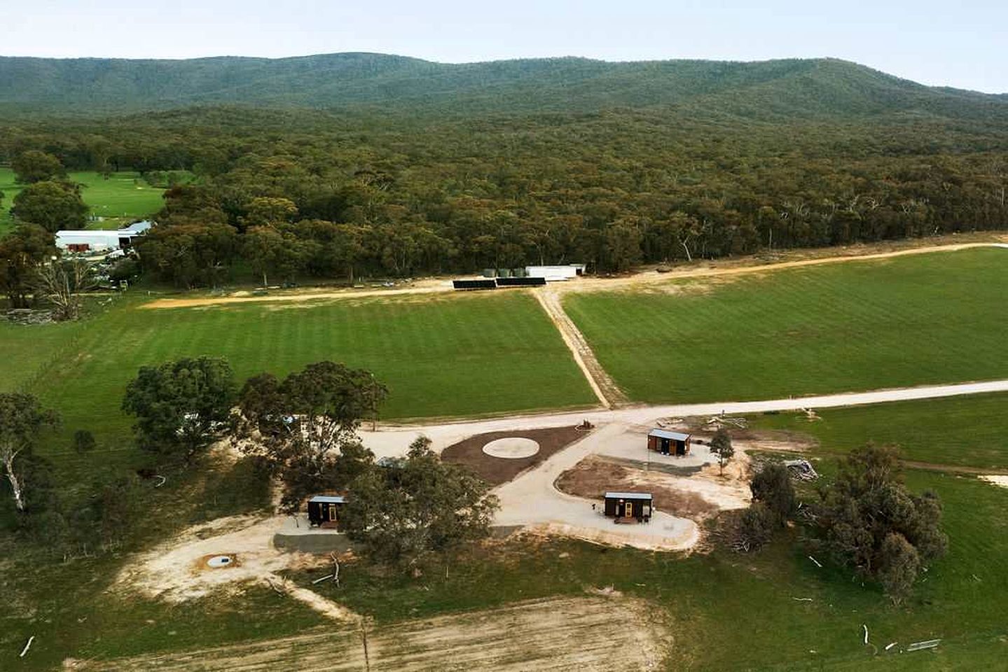 An aerial view of a property with multiple buildings, green fields, and a hilly landscape in the background.