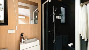 Un baño moderno con un mueble de tocador de madera, un box de ducha de vidrio y una toalla blanca colgada en la puerta.