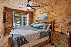 Ein Schlafzimmer einer Holzhütte mit einem Bett, einem Nachttisch, einem Gemälde und einem Deckenventilator.