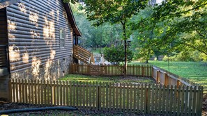A log cabin with a stone foundation, a wooden deck, and a fenced yard. - Cozy 2 Bed 2 Bath River Cabin Hot Tub Ellijay GA Blue Ridge Mt Pet Friendly (Ellijay)