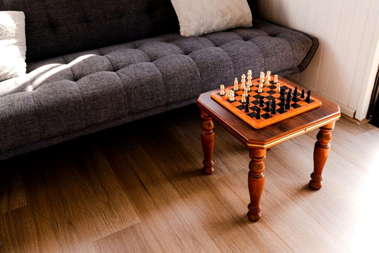 A chessboard on a wooden table with a dark sofa in the background.