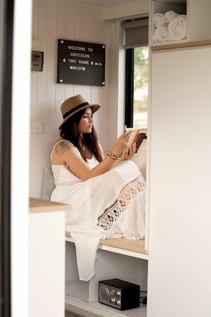 A person sitting by a window in a cozy room with a sign that reads 'Welcome to Odysseyan Tiny Home Enjoy.'