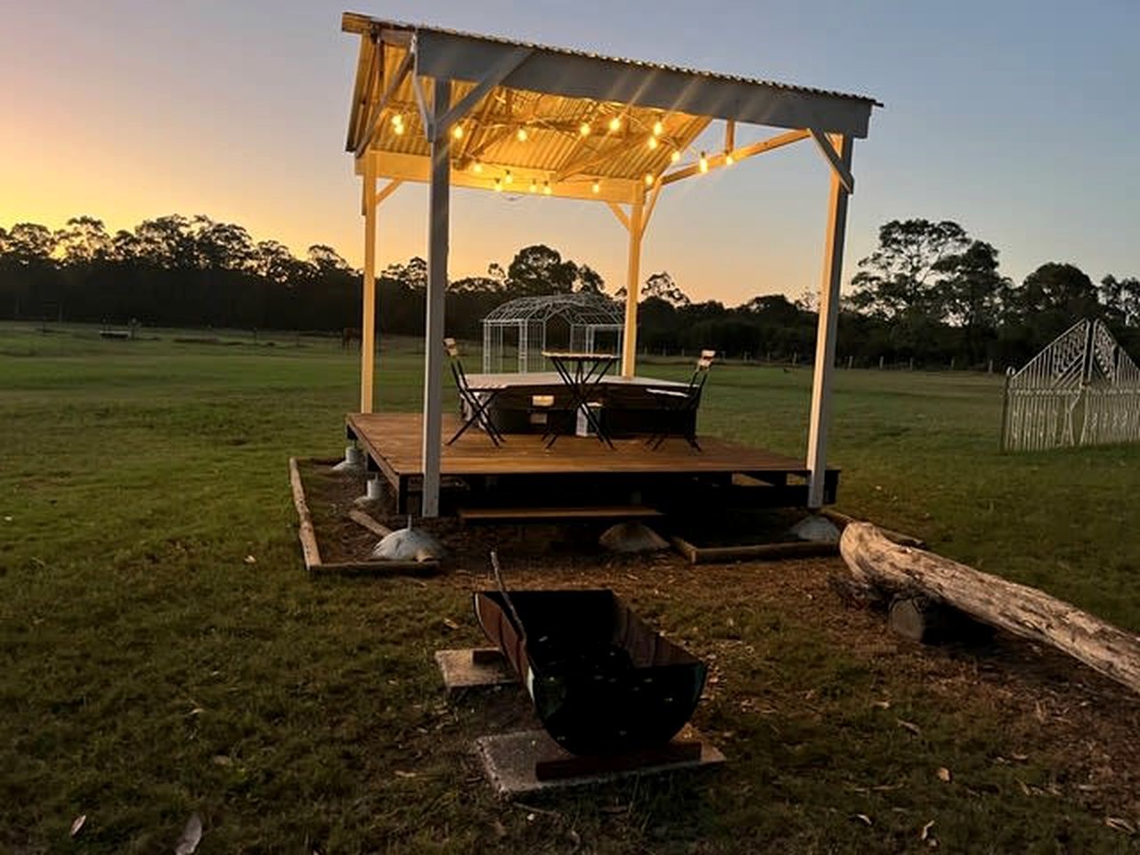An outdoor gazebo with a table and chairs, surrounded by a grassy field.