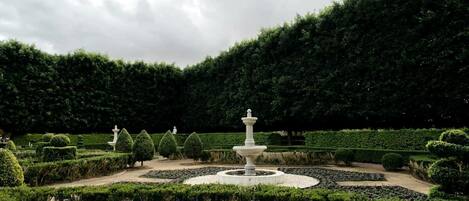 Ein formeller Garten mit einem zentralen Brunnen, geschnittenen Hecken und vielfältigen Pflanzen.