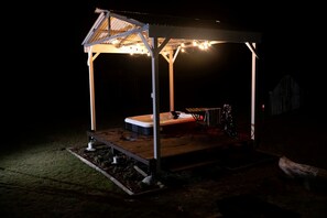 A covered outdoor hot tub area with a wooden deck, metal frame, and string lights.