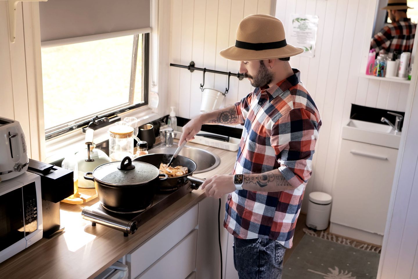 A person cooking in a modern kitchen with a microwave, toaster, and a pot on the stove.