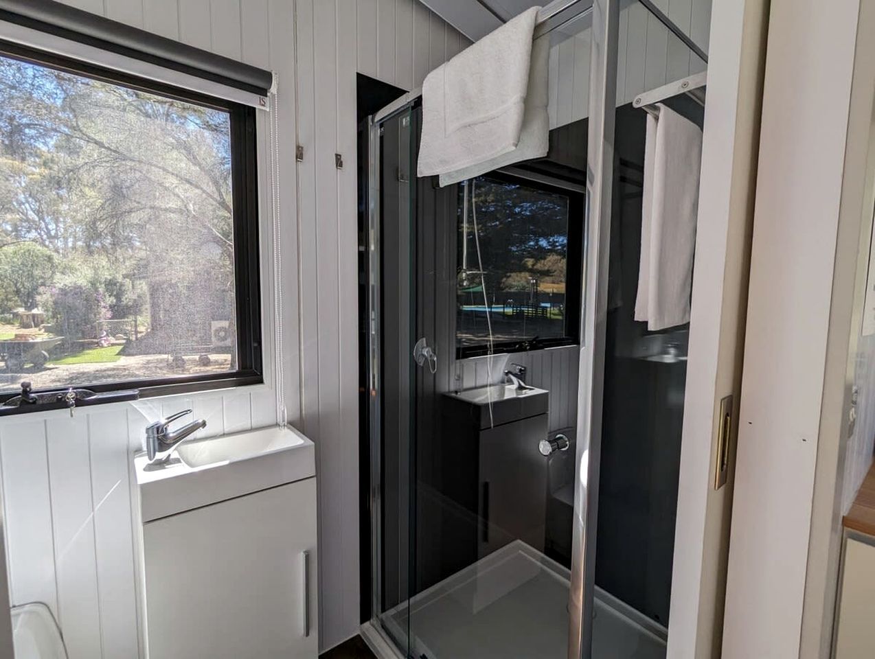 A modern bathroom with a glass shower enclosure, a white sink, and a window providing a view of the outdoors.