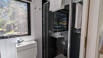 A modern bathroom with a glass shower enclosure, a white sink, and a window providing a view of the outdoors.