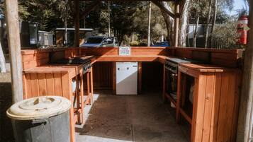 An outdoor wooden barbecue area with a sink, a refrigerator, and a trash can.