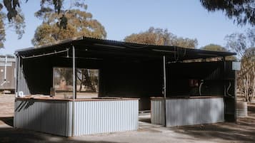 A metal structure with a roof and a bench area, surrounded by trees.