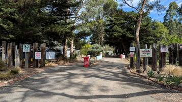 A gated entrance to a park with wooden posts, signs, and a red trash bin.