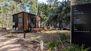 A modern tiny cabin with a wooden exterior, a picnic table, and a sign indicating nearby cabins and Tiny accommodations.
