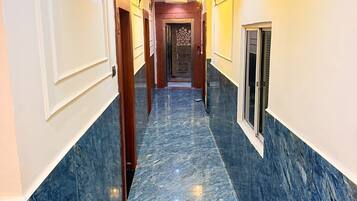 A hallway with marble flooring, wall-mounted lights, and a door at the end.