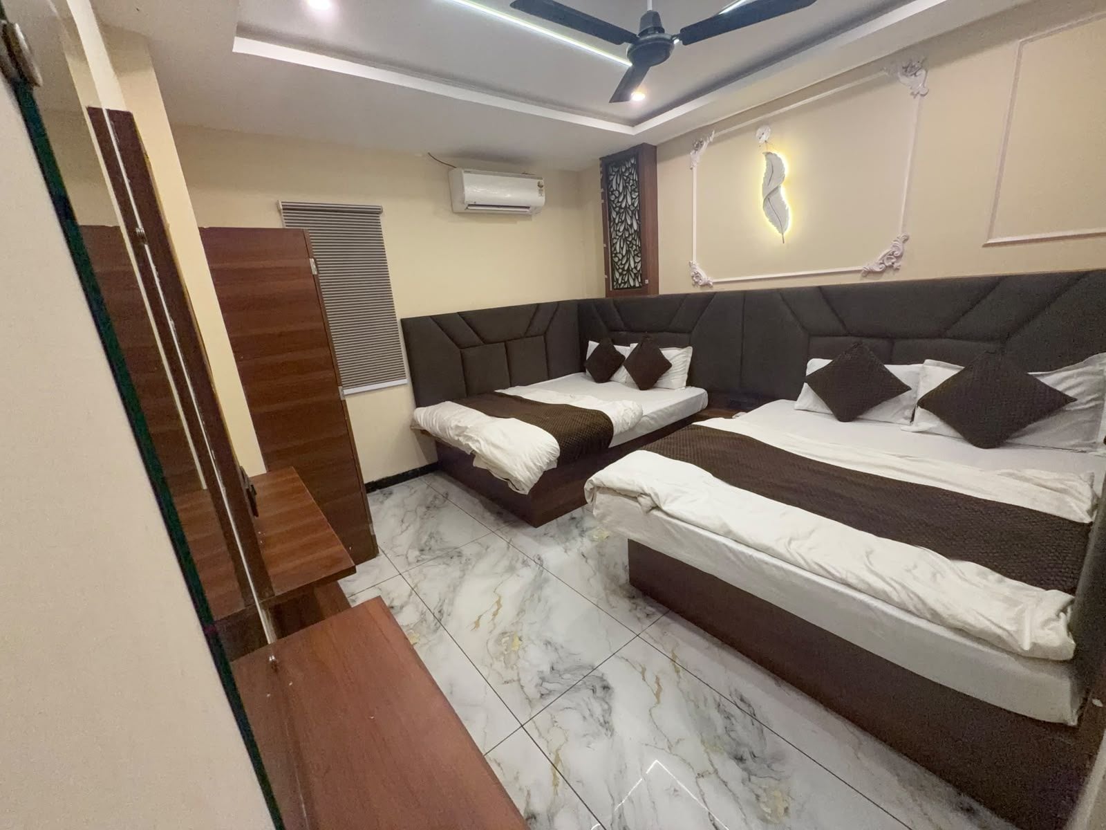 A hotel room with two beds, a ceiling fan, an air conditioning unit, and a decorative wall panel.