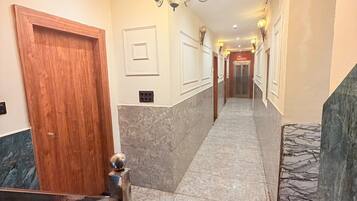 A hotel hallway with a wooden door, marble flooring, a metal railing, and a chandelier.