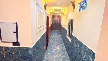 A hallway with marble flooring, wall-mounted light fixtures, and a door at the end.