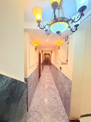 Un pasillo con piso de mármol, luces empotradas en la pared y un elemento decorativo en el techo.