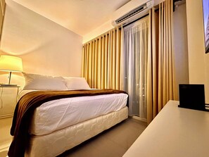 A hotel room with a bed, bedside table, lamp, air conditioning unit, and curtains. - Luxury Seaside Sunset View Mall of Asia with Free Parking (Pasay City)